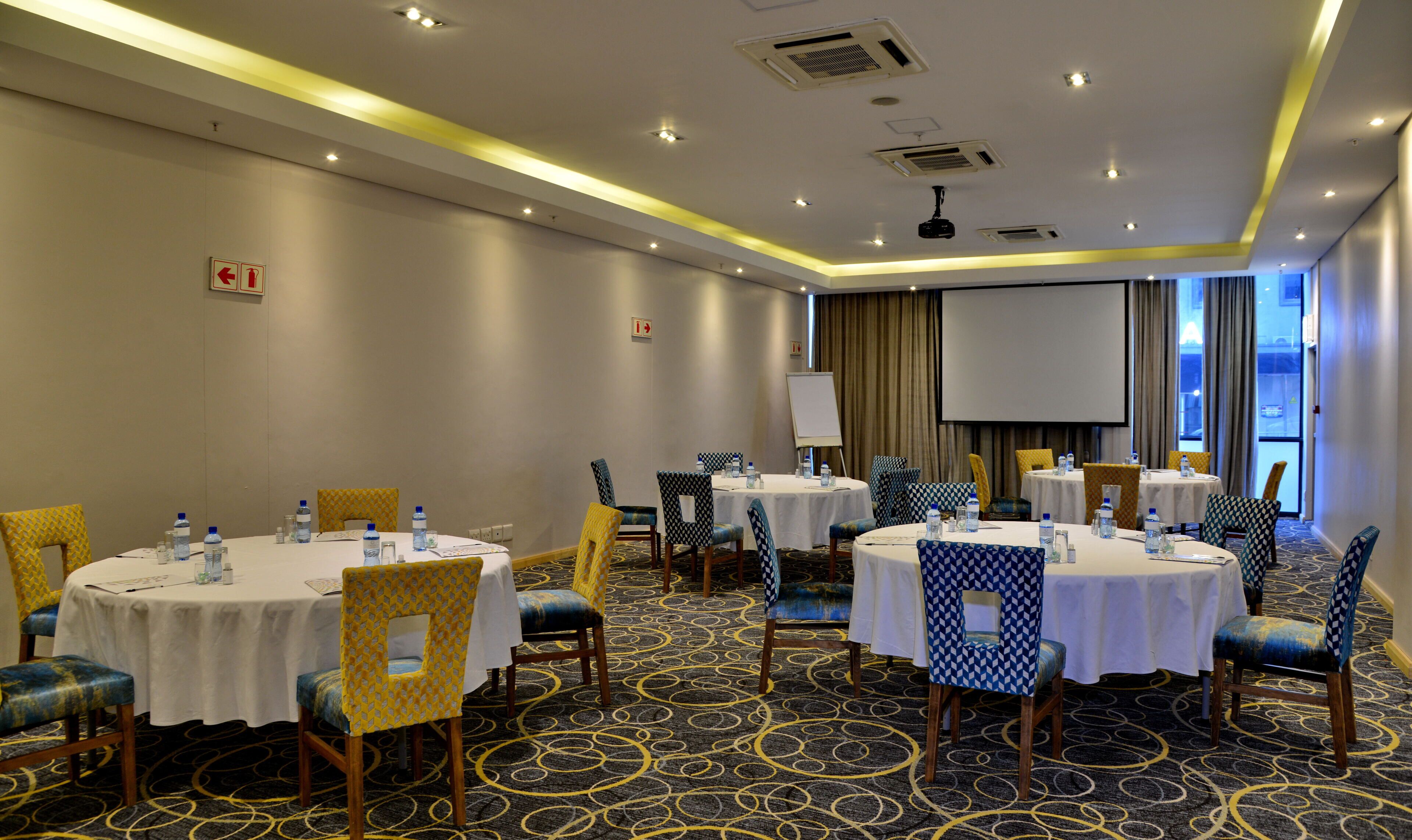 A conference room with multiple tables, chairs, and a projector screen.
