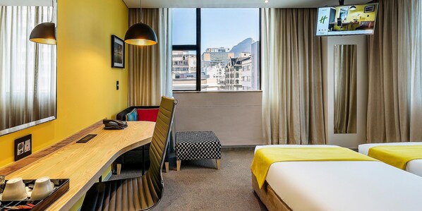 A hotel room with a desk, two beds, a chair, and a TV.