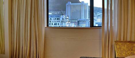 A hotel room with a large window offering a city view, a bed, a chair, and an ottoman.