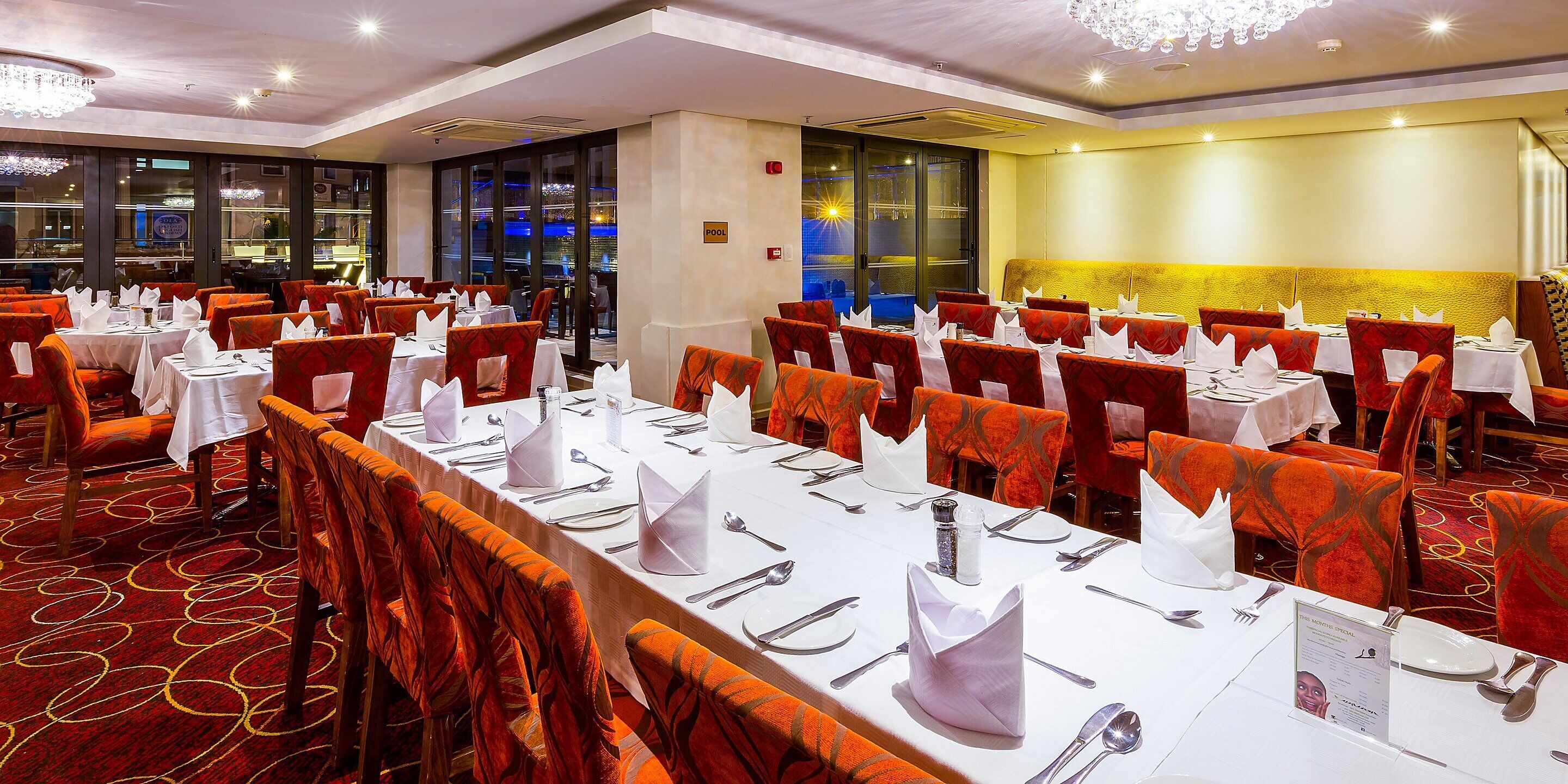A banquet hall with tables set for dining, red upholstered chairs, and a chandelier.