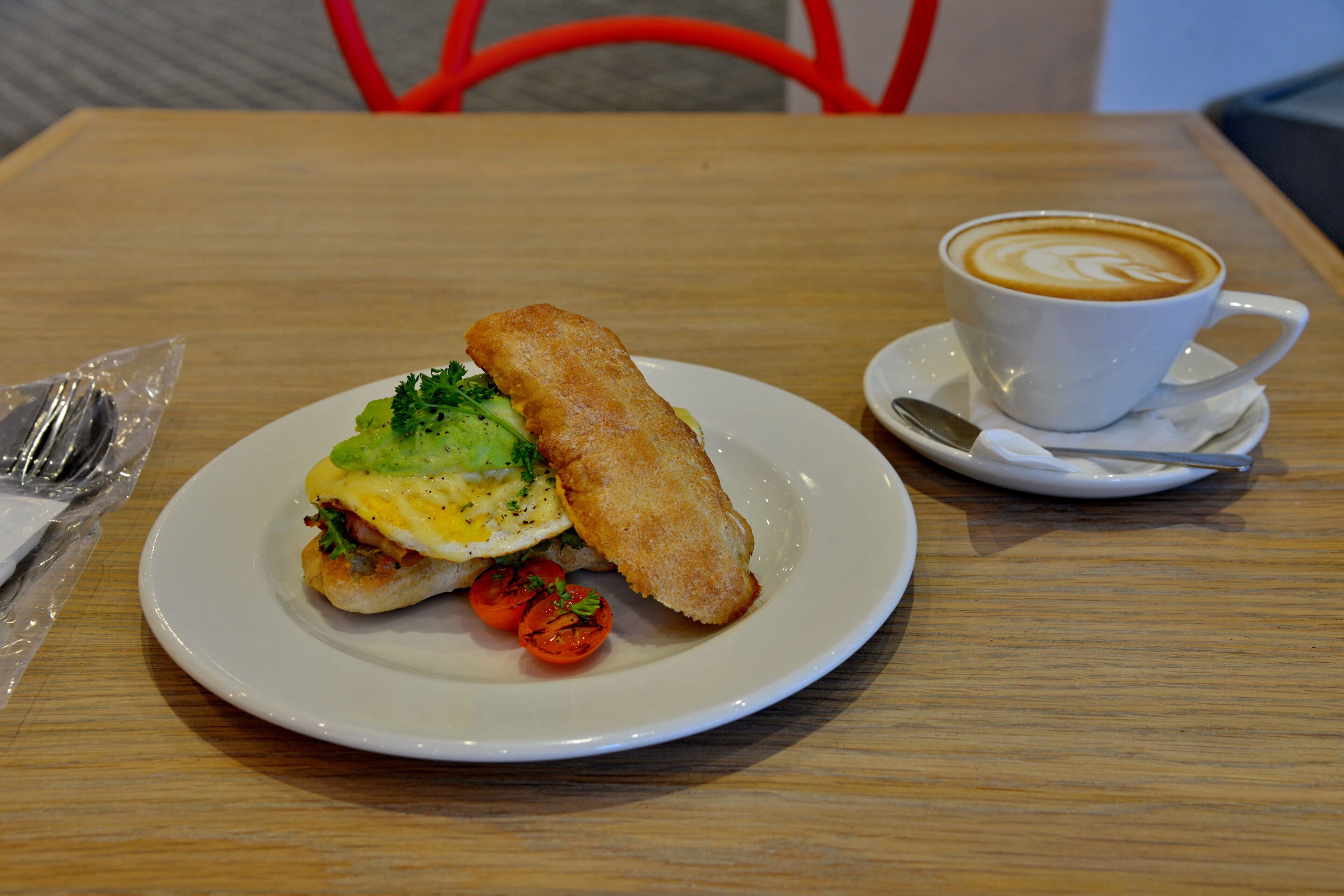 A plate with a sandwich and two grilled tomatoes, a cup of coffee, and a spoon on a wooden table.