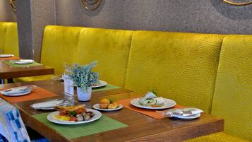 L’intérieur d’un restaurant avec des tables en bois, des banquettes jaunes et moelleuses, et différentes assiettes remplies de plats.