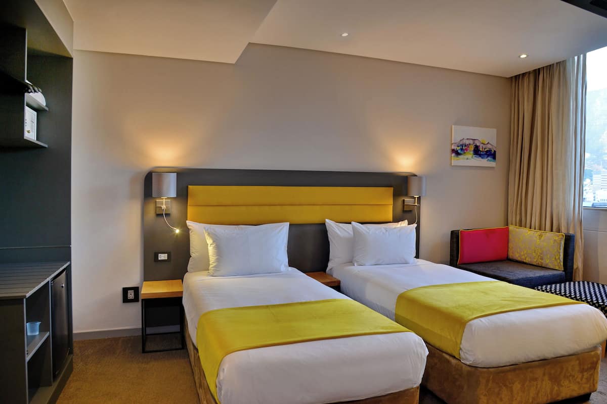 A hotel room with two beds, a sofa, a TV, and a painting on the wall.
