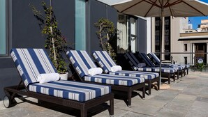 Une rangée de fauteuils de jardin en osier, dotés de coussins à rayures, disposés sur une terrasse en pierre.