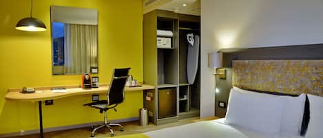 A hotel room with a bed, a desk, a chair, a wardrobe, and a mirror.