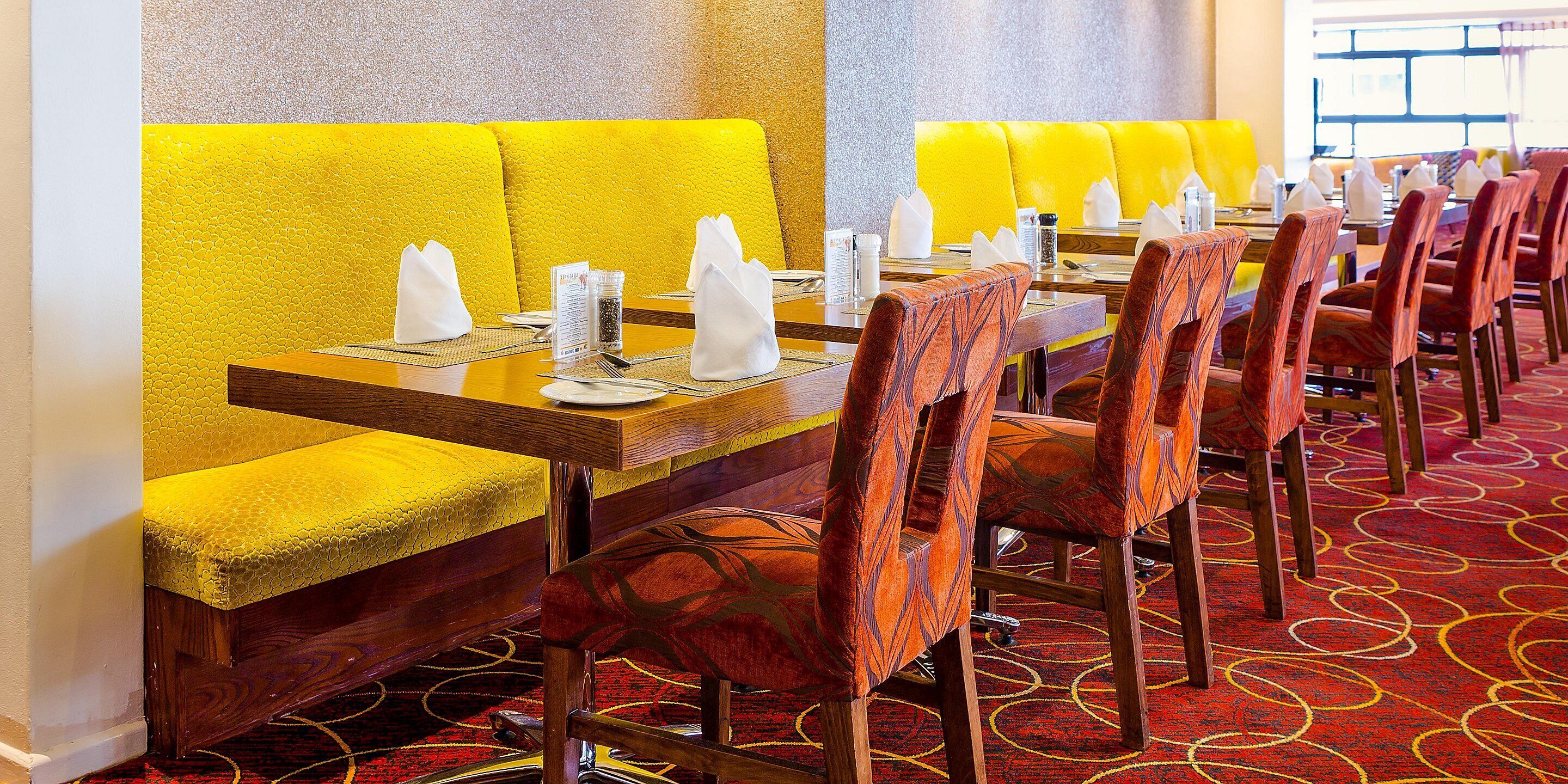 A restaurant with yellow booths and red upholstered chairs, arranged around a long wooden table with place settings.