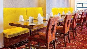 Un restaurante con asientos de cuero amarillo y sillas tapizadas rojas, dispuestas alrededor de una larga mesa de madera con mantelería.