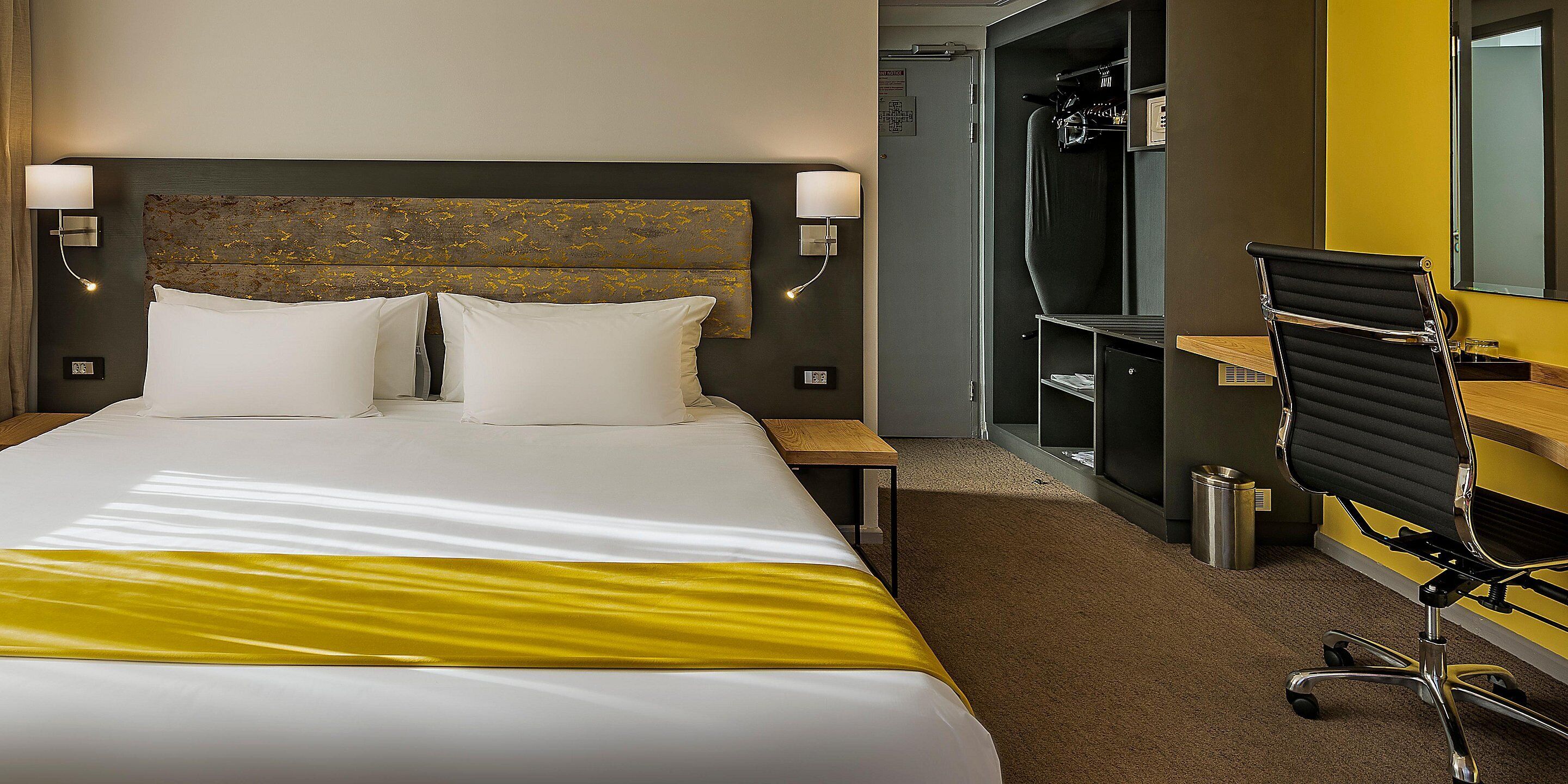 A hotel room with a large bed, two bedside tables, a desk, and a chair.
