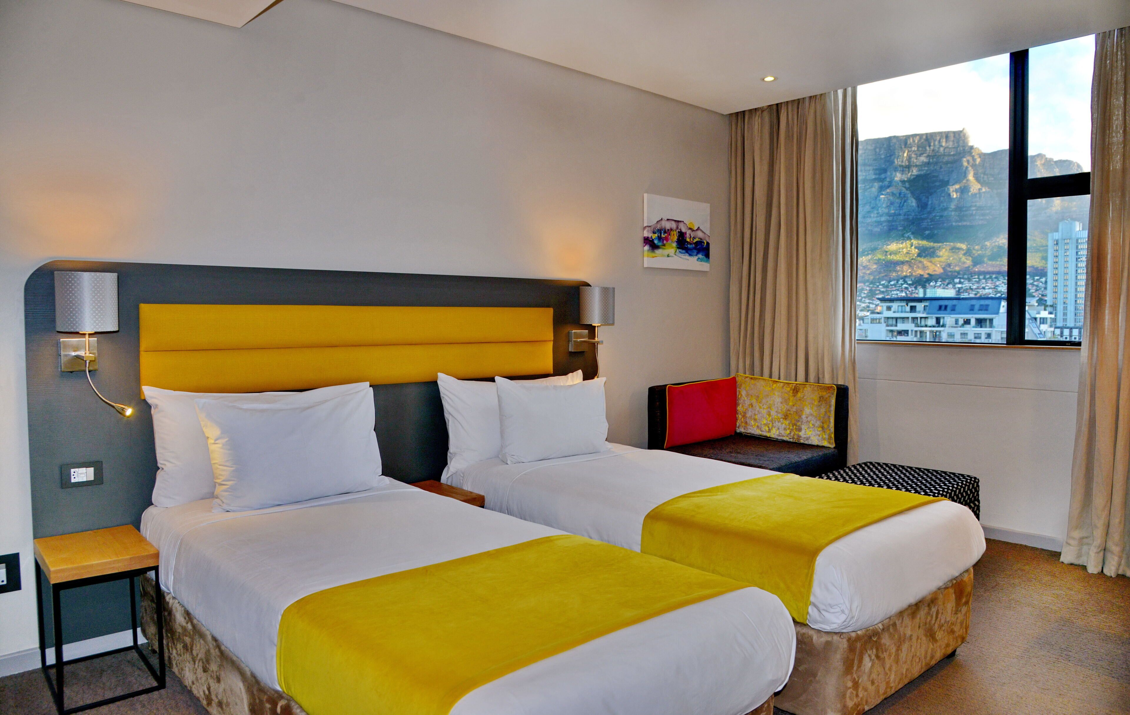 Habitación de hotel con dos camas, una mesita de noche, un escritorio y ventana con vista a la ciudad.