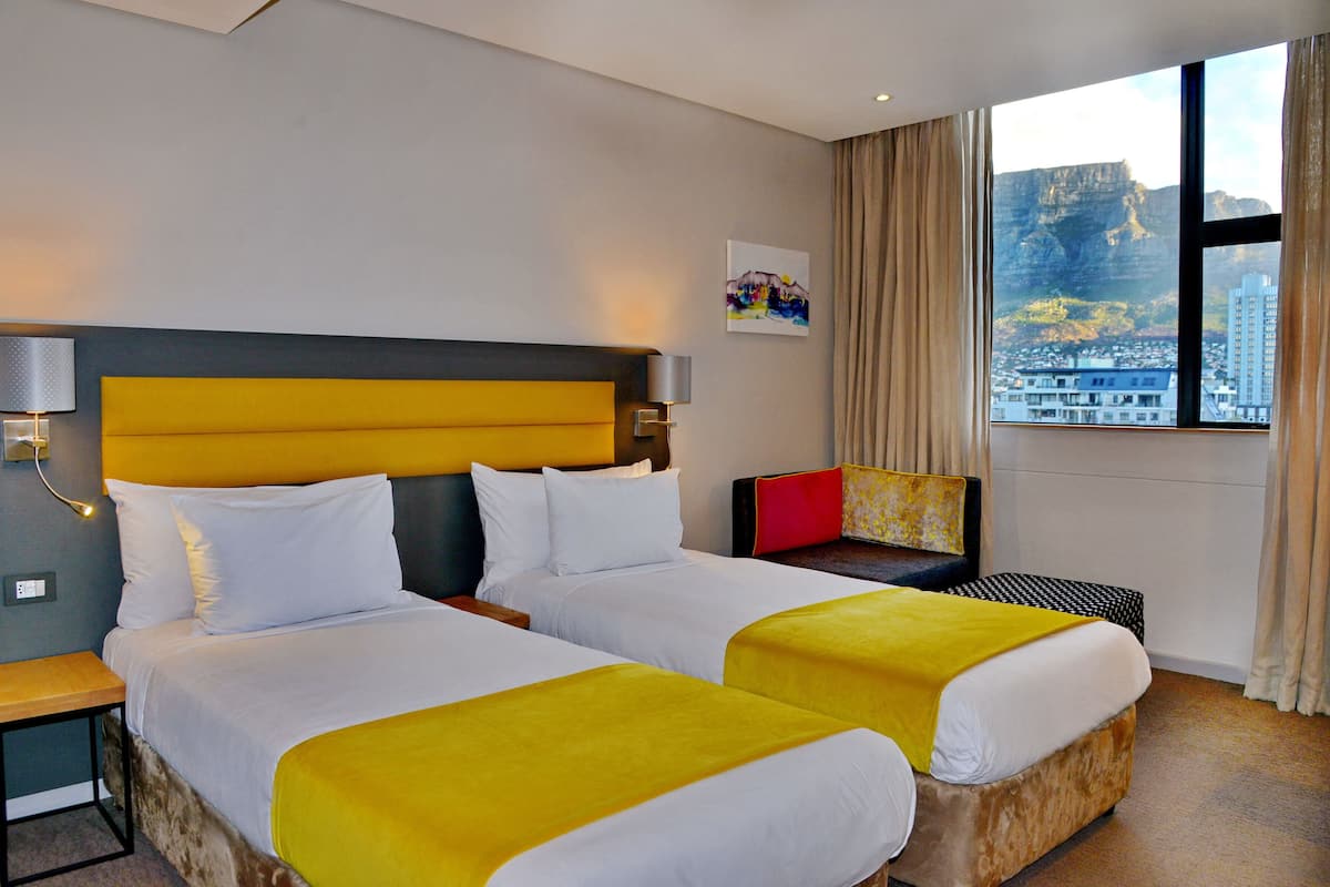A hotel room with two beds, a nightstand, a desk, and a window with a city view.