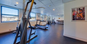 A gym with treadmills, weight machines, and a large window offering a city view.