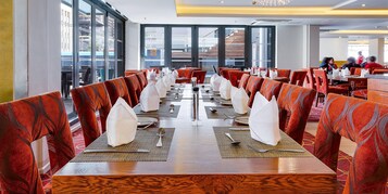 A restaurant with high tables and red upholstered chairs, large windows, and a view of buildings outside.