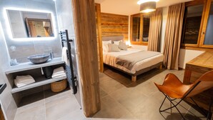 Een moderne hotelkamer met een groot bed, een houten hoofdeinde, een spiegel met houten lijst, een ingebouwd wastafelmeubel en een houten eettafel.