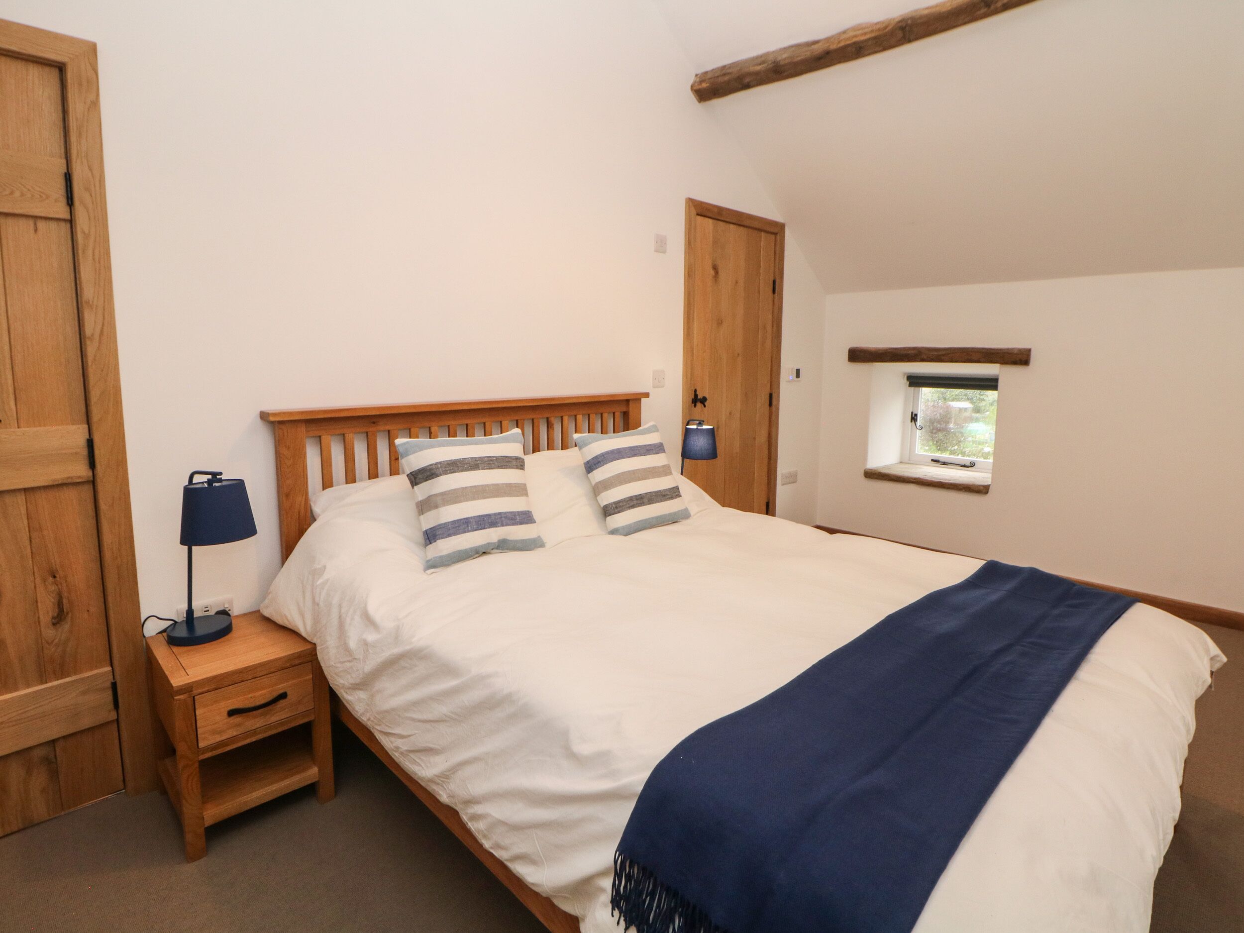 A bedroom with a wooden bed, two bedside tables with lamps, a small window, and a wooden door.