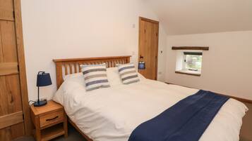 A bedroom with a wooden bed, two bedside tables with lamps, a small window, and a wooden door.