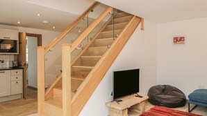 Una sala de estar moderna con una escalera de madera, un televisor de pantalla plana, un sillón de orejas y una alfombra roja.