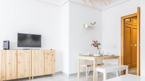 Una habitación moderna con un armario de madera, un televisor, una mesa de comedor con sillas y una puerta de madera.