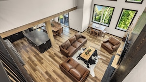 A spacious living area with a high ceiling, wooden flooring, and large windows offering a view of greenery.