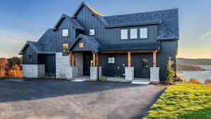 A modern two-story house with a stone foundation, a dark roof, and a driveway leading to the entrance.