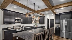 Une cuisine moderne avec des meubles de couleur sombre, des appareils en acier inoxydable et un îlot central doté de tabourets de bar.