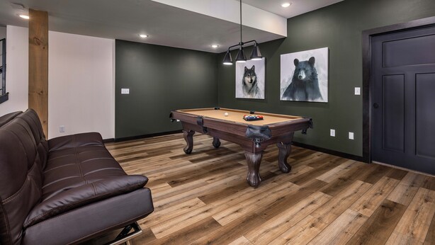 A room with a pool table, a brown leather couch, and two wall-mounted paintings of wolves.