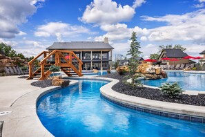 A swimming pool with a wooden deck, a small building with a balcony, and red umbrellas. - Luxury Lakefront Villa w/ FREE Kayaks, Pools & Resort-Style Amenities (Kimberling City)
