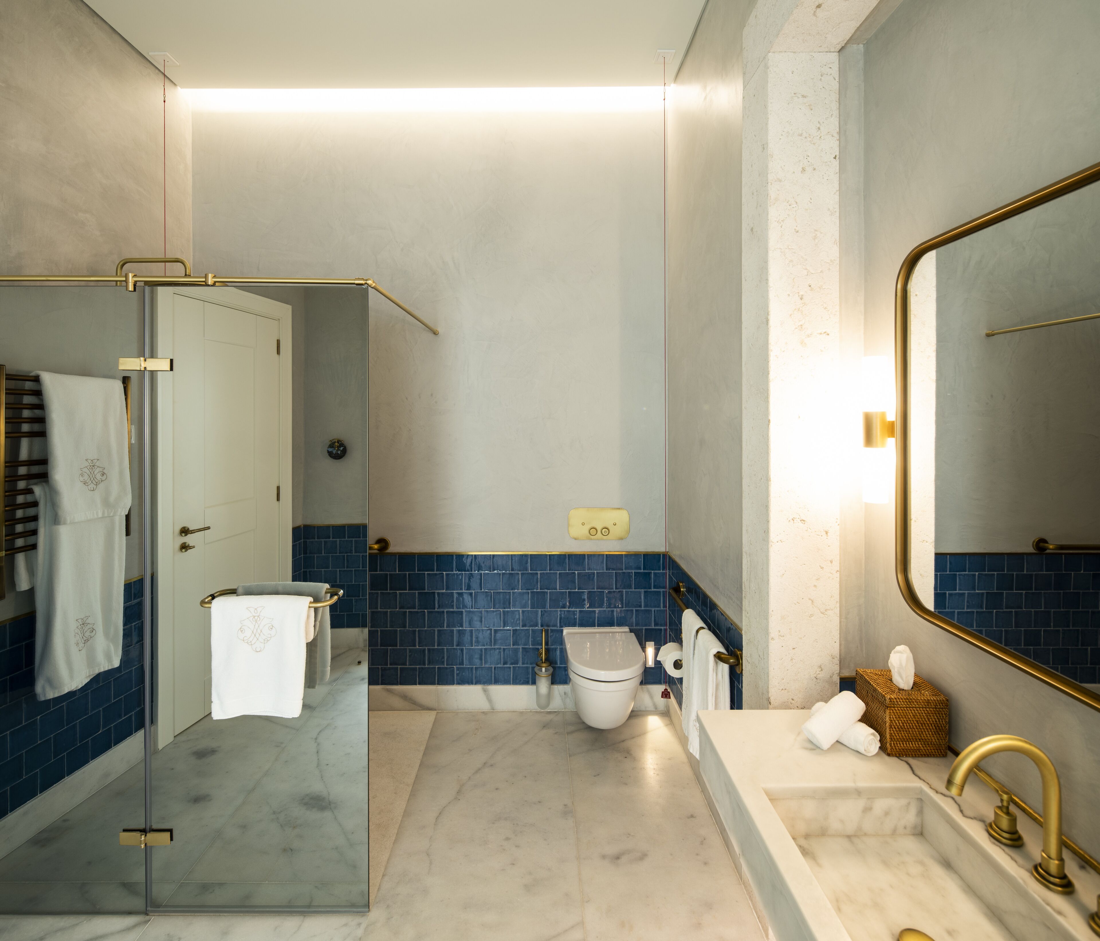 Un baño moderno con cabina de ducha de vidrio, inodoro blanco, lavamanos con grifo dorado y un espejo grande.