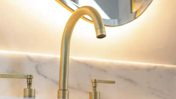 Un baño con grifo dorado, encimera de mármol y espejo redondo.