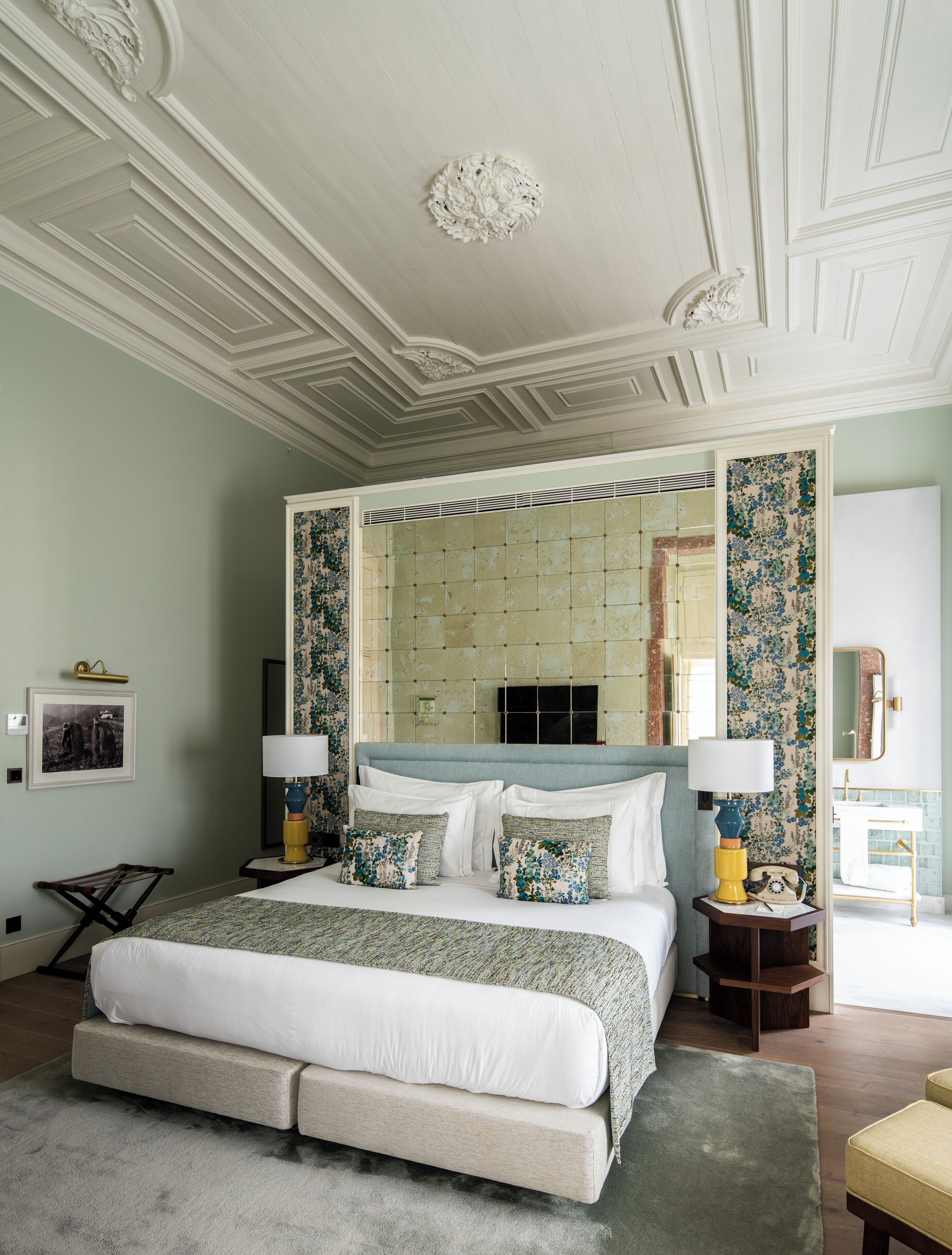 A spacious bedroom with a large bed, two bedside tables with lamps, a mirror, and a view of the bathroom.