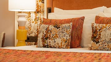 Una cama bien hecha con almohadas y un plaid de estampado floral, una lámpara de noche y una mesita de noche con una lámpara amarilla.