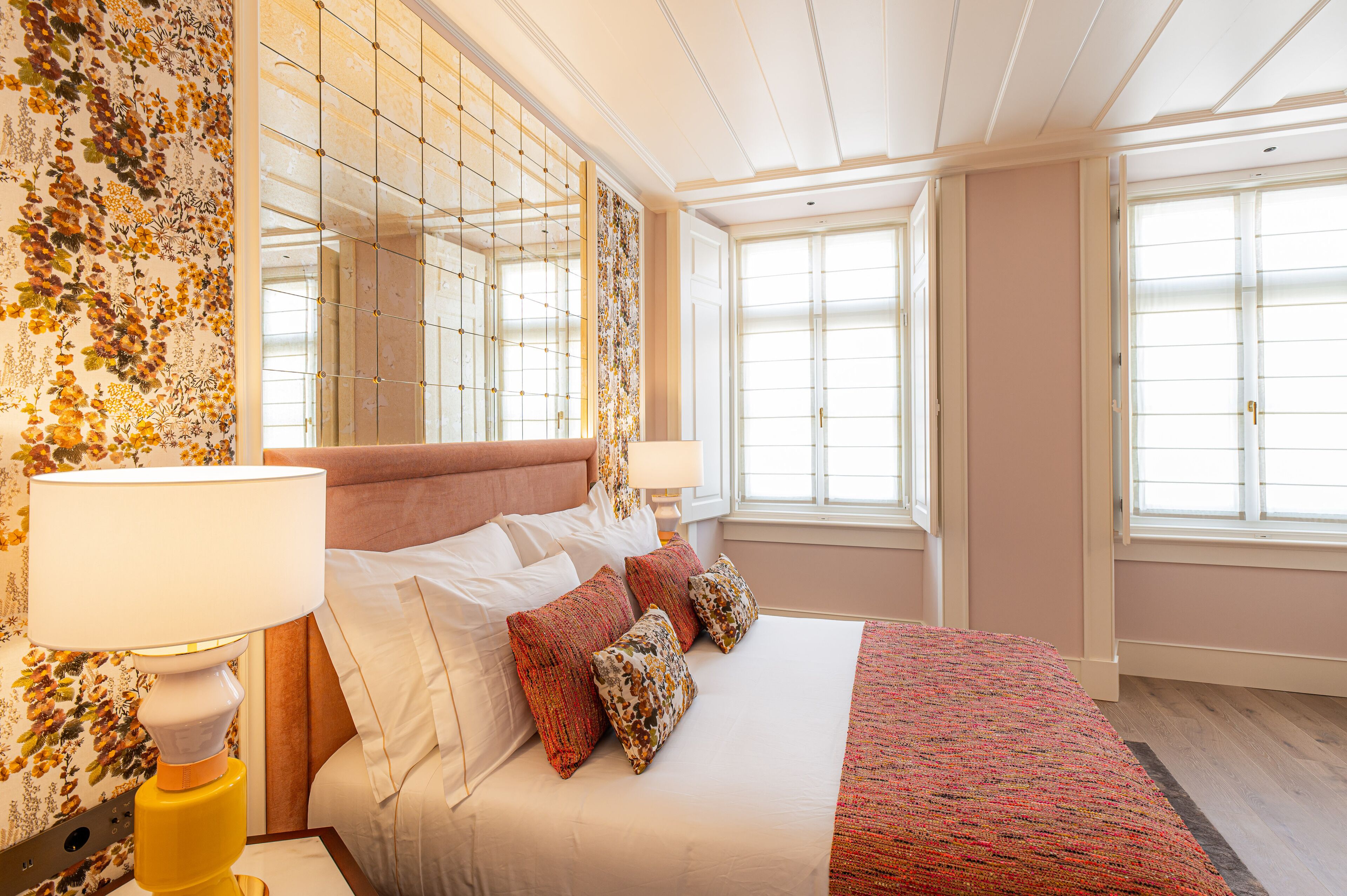 A hotel room with a large bed, floral wallpaper, and a view of the city.