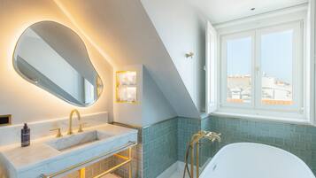 Une salle de bain moderne avec un grand miroir, deux vasques, une baignoire et une fenêtre donnant sur la ville.