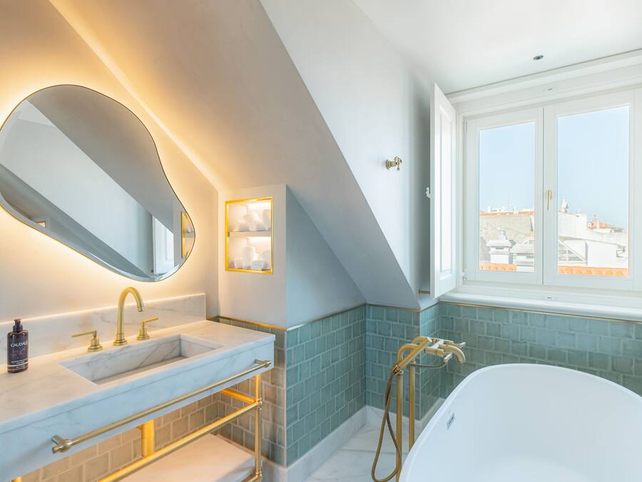 A modern bathroom with a large mirror, dual sinks, a bathtub, and a window with a city view.