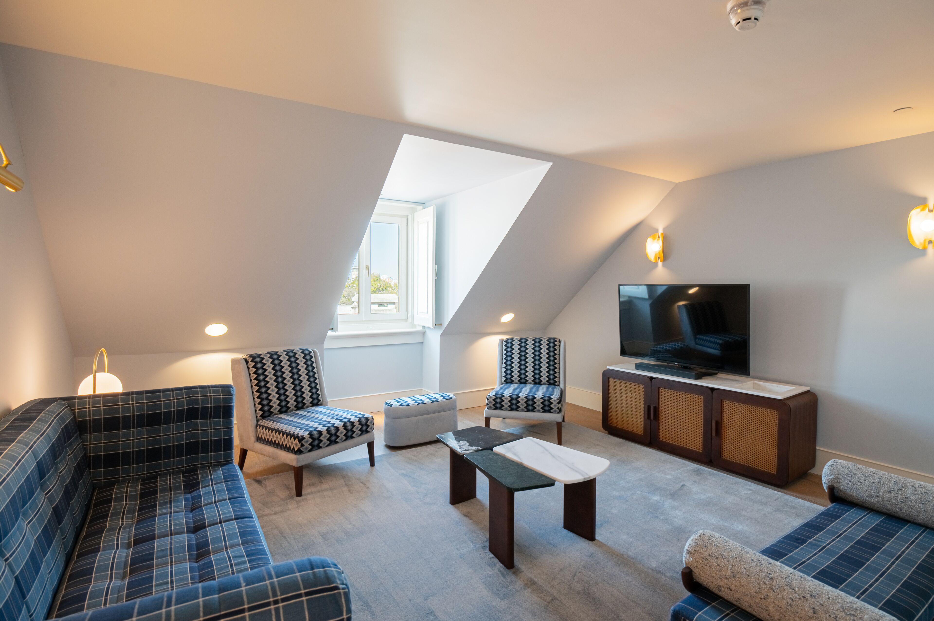 Un salon moderne de style loft, doté d’un plafond en pente, d’un téléviseur à écran plat et d’une variété de sièges, notamment un canapé, des fauteuils et un pouf.
