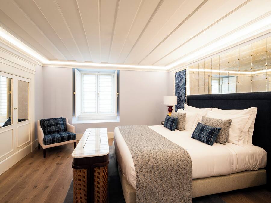 A bedroom with a bed, a nightstand, a chair, a window, and a mirror.