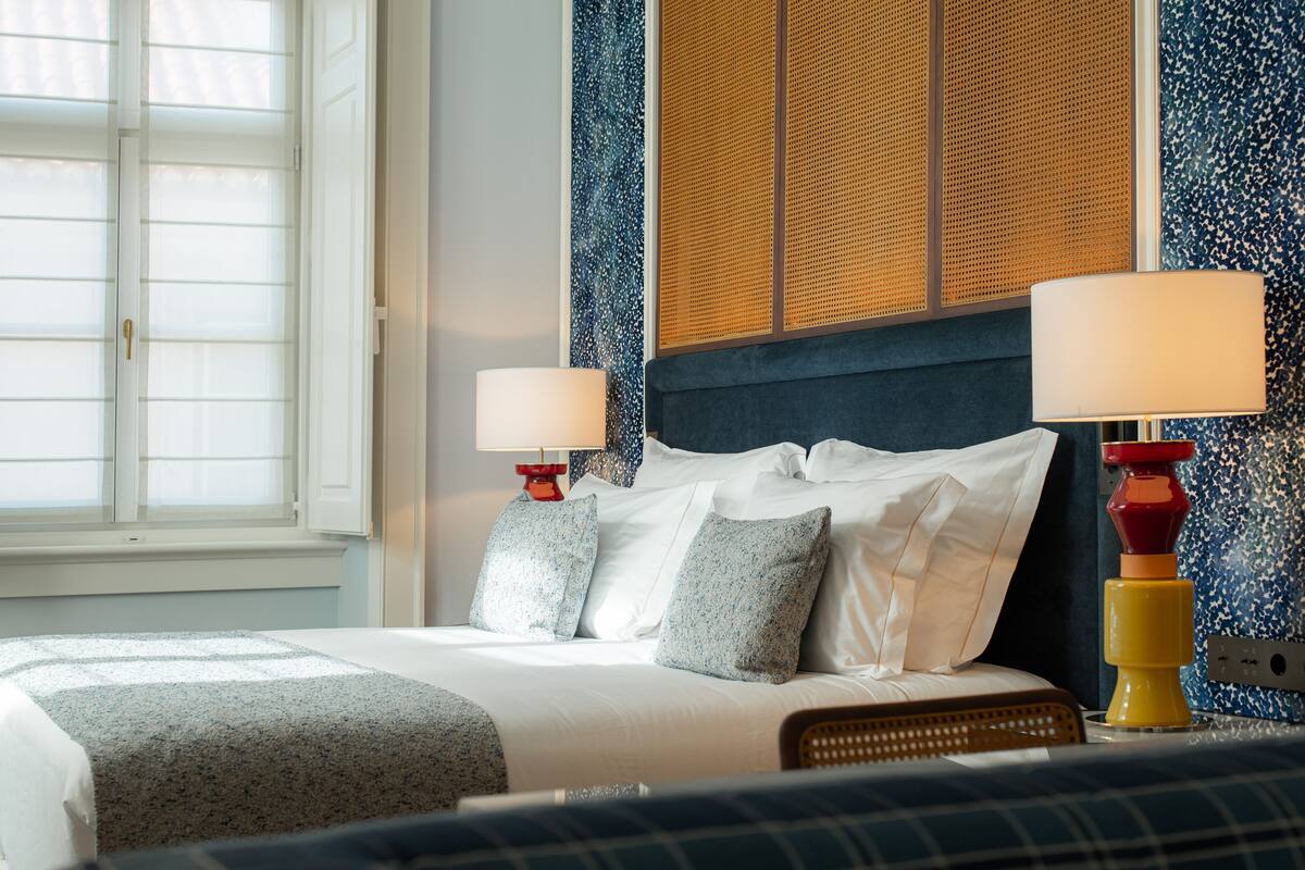 Ett hotellrum med en säng, två sängbord med lampor, ett fönster och en vägg med en intressant yta.