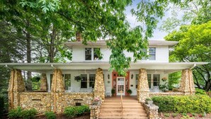 A two-story house with a stone facade, a front porch, and a brick pathway leading to the entrance.