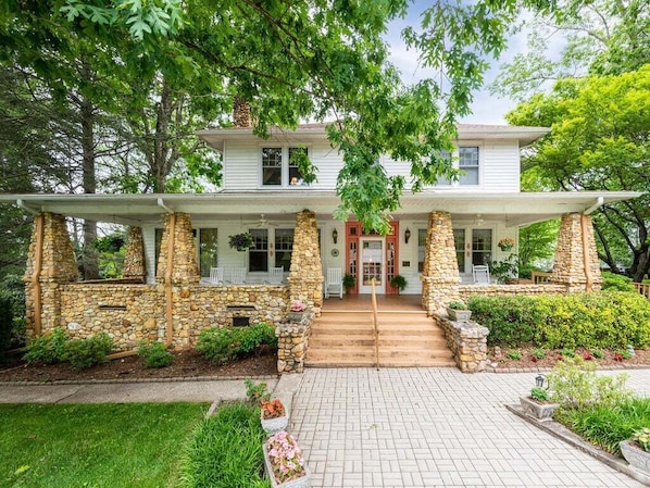 A two-story house with a stone facade, a front porch, and a brick pathway leading to the entrance.