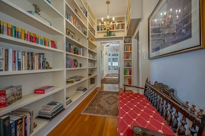 A library with bookshelves on both sides, a wooden floor, and a red upholstered bed with a wooden headboard.