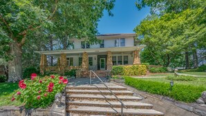 A two-story house with a stone facade, a front porch, and a staircase leading to the entrance.