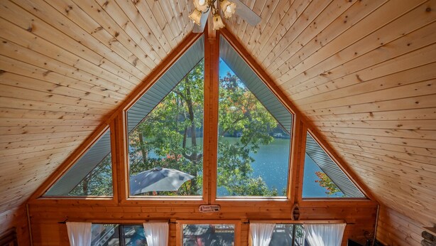 Une cabane en bois dotée d’une grande fenêtre triangulaire qui offre une vue sur un lac entouré d’arbres.