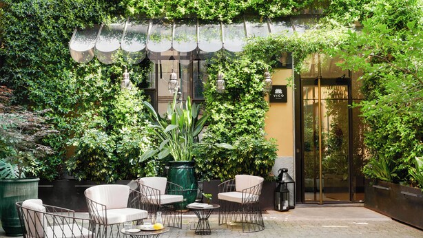 An outdoor seating area with wicker chairs and tables, surrounded by lush greenery and potted plants. - Vico Milano (Milan)