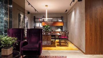 A modern living room with a marble column, a purple armchair, a glass coffee table, a red rug, and a dining area with a wooden table and chairs.