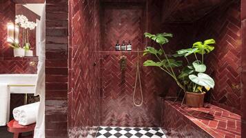 A bathroom with a herringbone-patterned wall, a white towel on a red stool, a black and white checkered floor, and a potted plant.