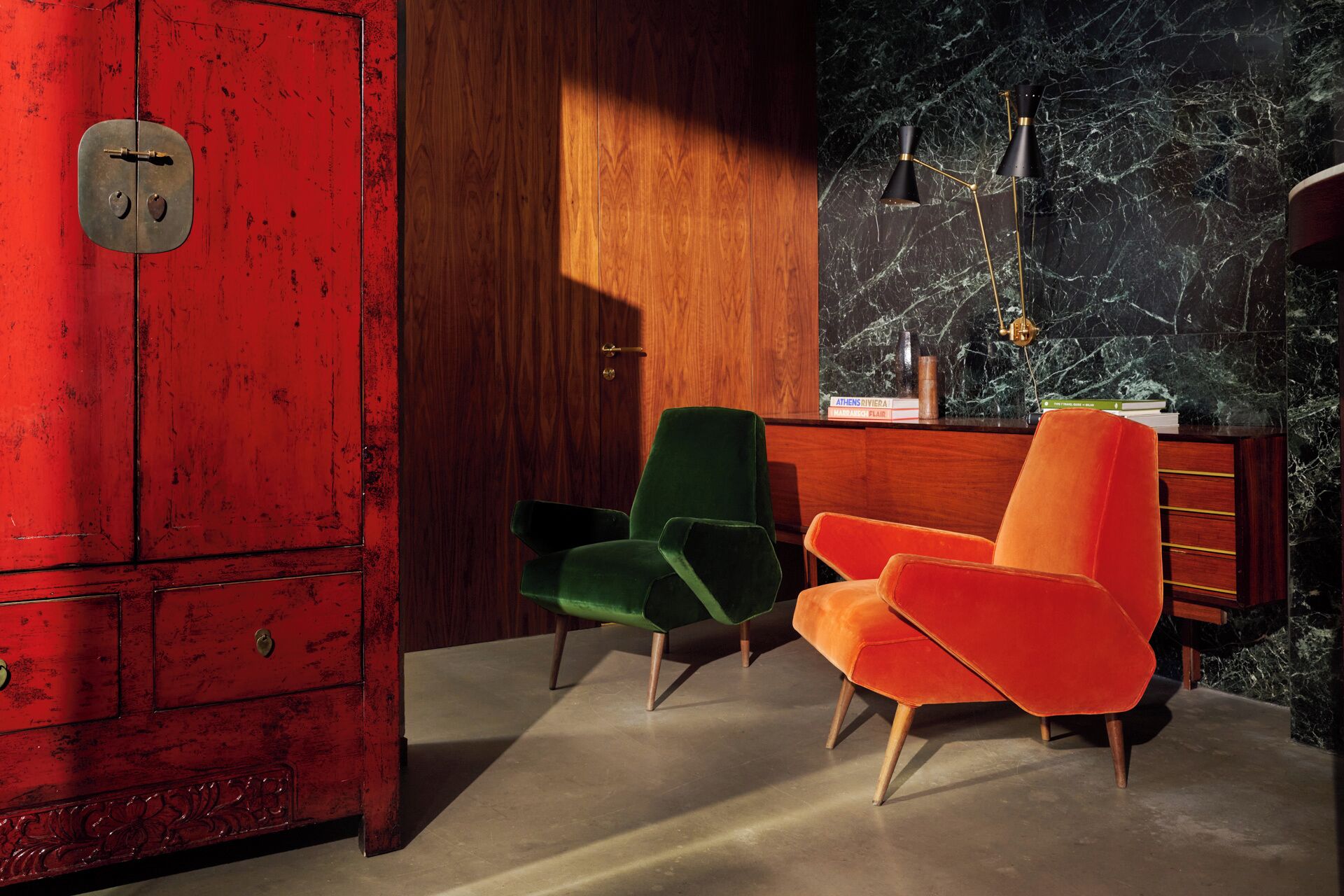 A room with a red cabinet, two chairs, a wooden desk, and a marble wall.