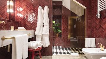 A modern bathroom with a herringbone patterned wall, a gold vanity, a white bathtub, and a red stool.