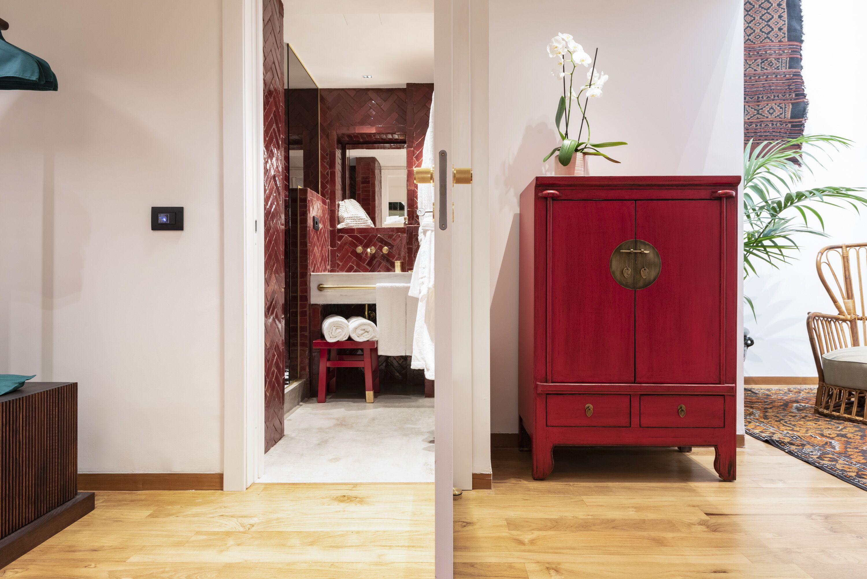 Un pasillo con un armario rojo, suelo de madera y un baño visible a través de una puerta abierta.