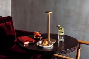 A round table with a glass of iced drink, a plate with a pastry, a red notebook, and a red cushion on a dark wooden chair. - Vico Milano (Milan)