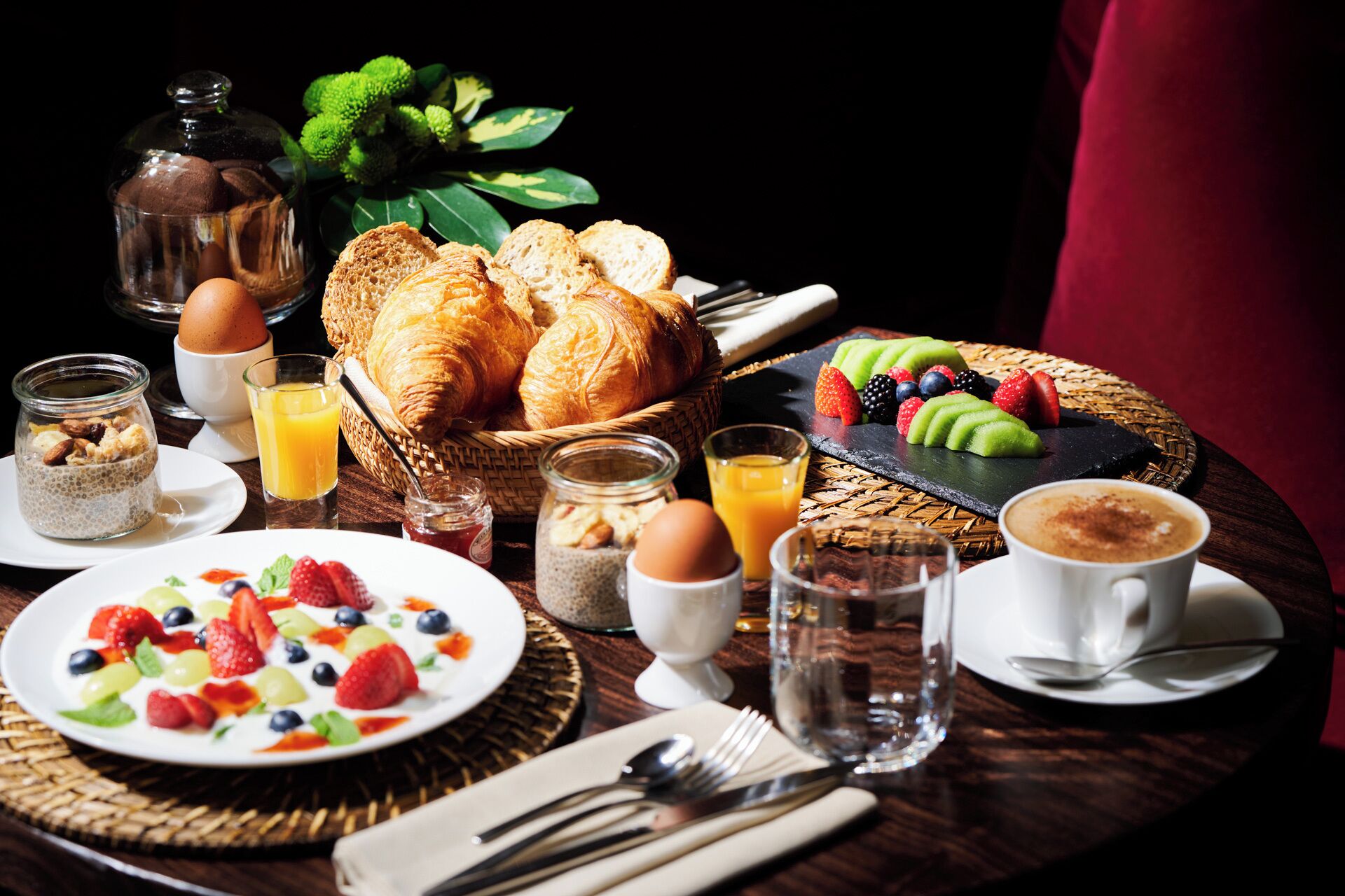 Un esmorzar amb croissants, fruita, iogurt i cafè sobre una taula de fusta.