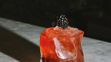 Ein Glas mit einem roten Getränk, Eiswürfeln und einer Brombeere auf einer Marmorplatte.